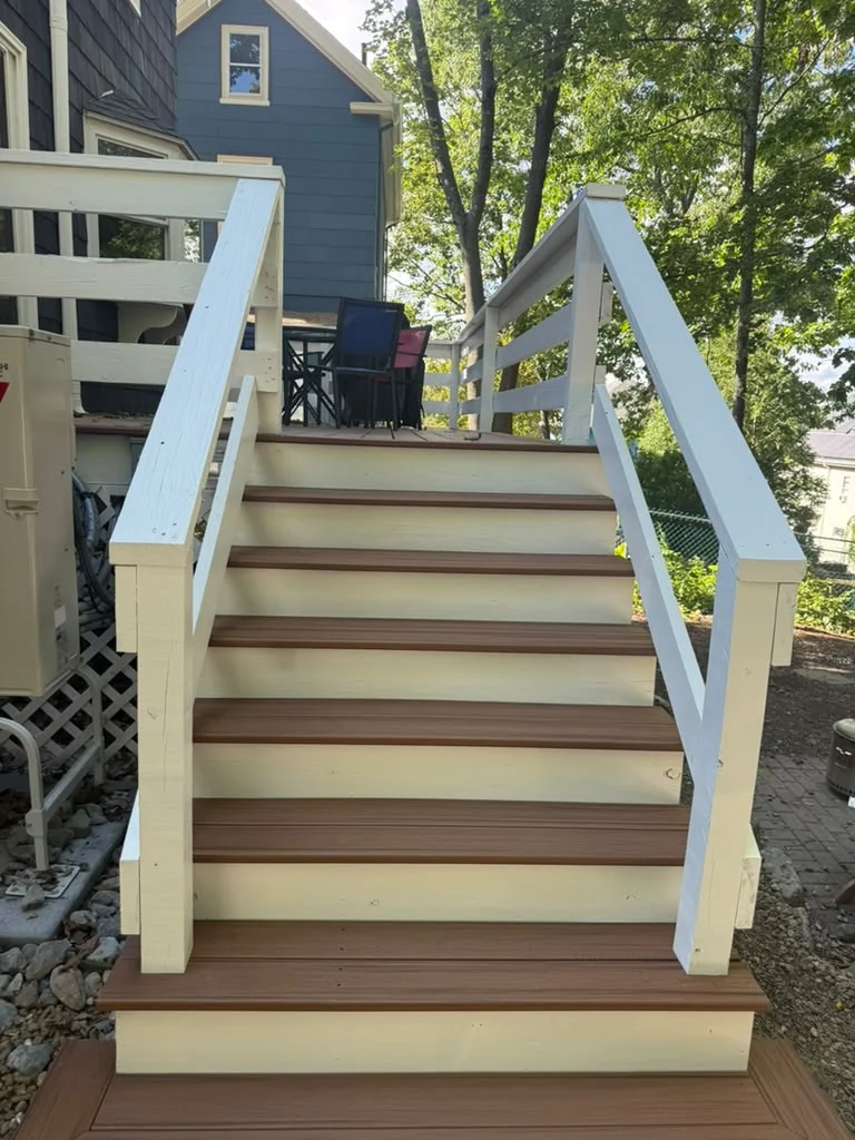 Outdoor stairs with white risers and brown treads leading to a deck with railings. by ALP Home Services in Somerville, MA