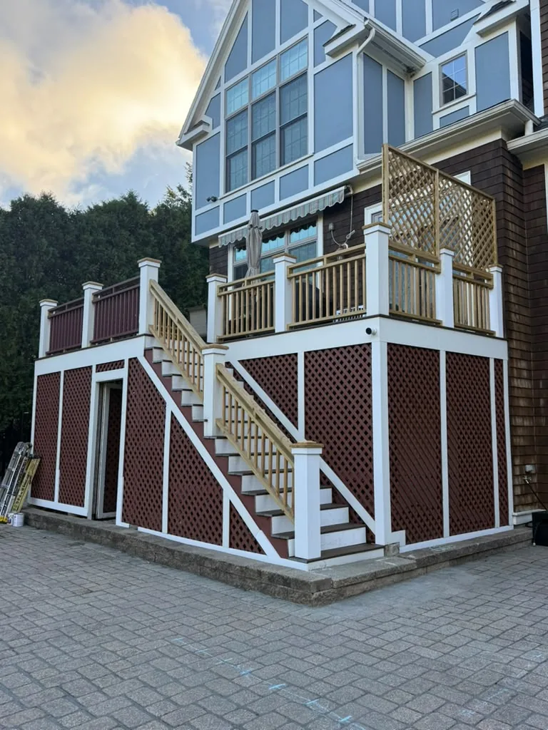 Before deck painting in Newton, MA: elevated two-level deck with new raw wood railings and red lattice skirting