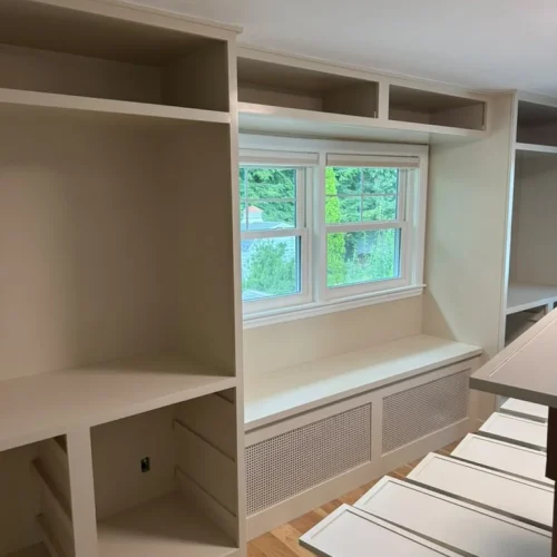 Custom built-in shelving, window seat, and radiator cover in a light neutral color. by ALP Home Services in Somerville, MA